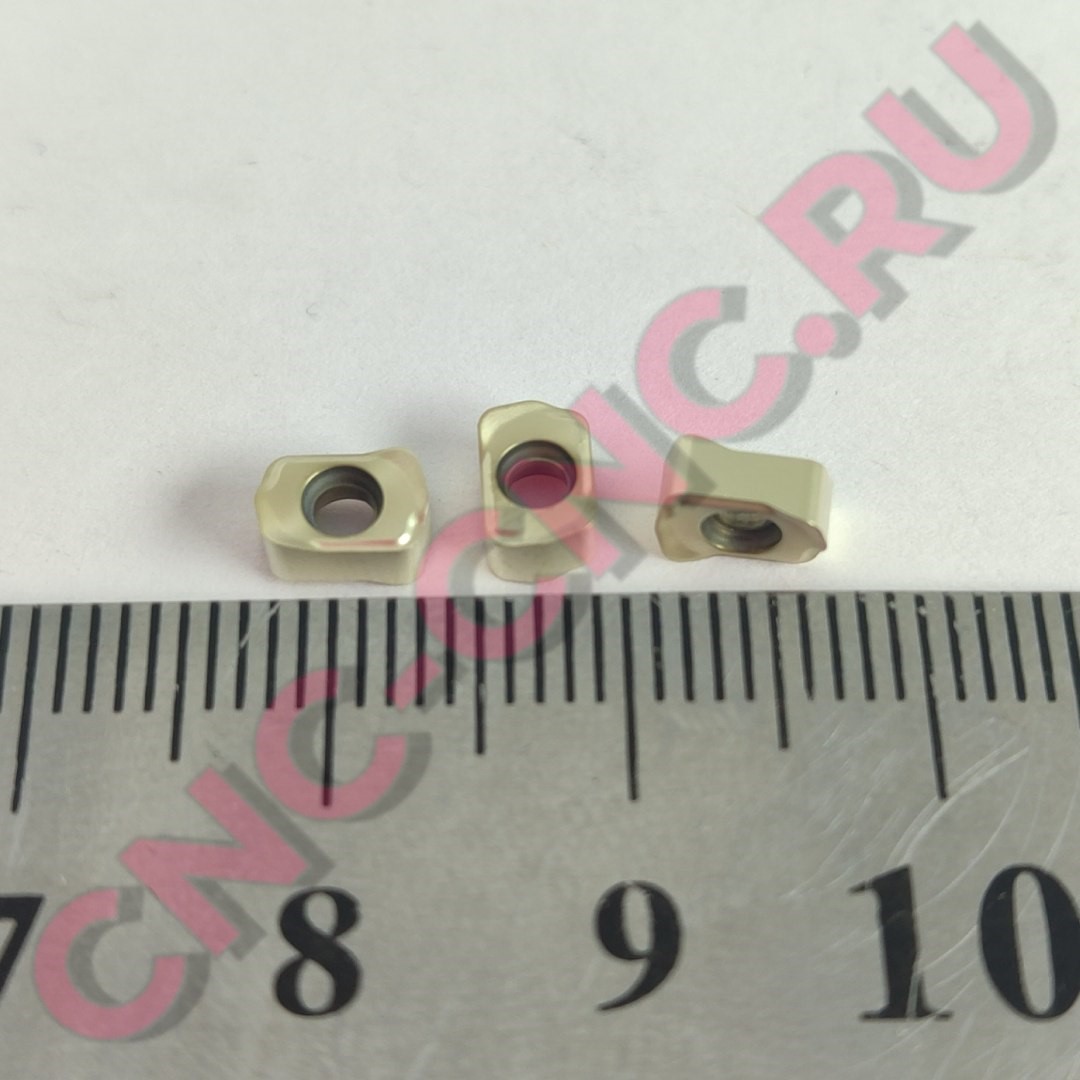 Three small square nuts with internal threading placed on a ruler for scale, light-beige in color.