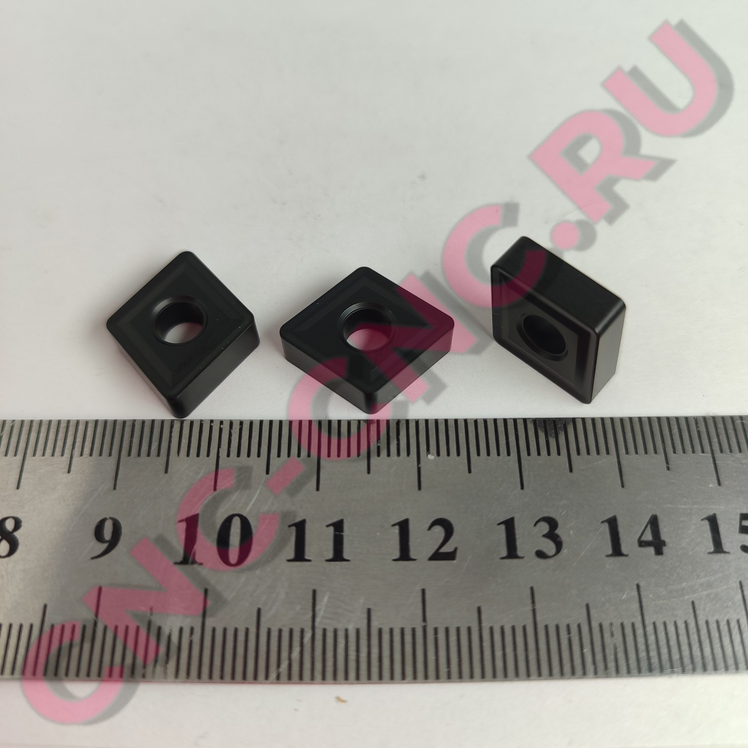 Three black square blocks with circular holes, arranged diagonally on a ruler background