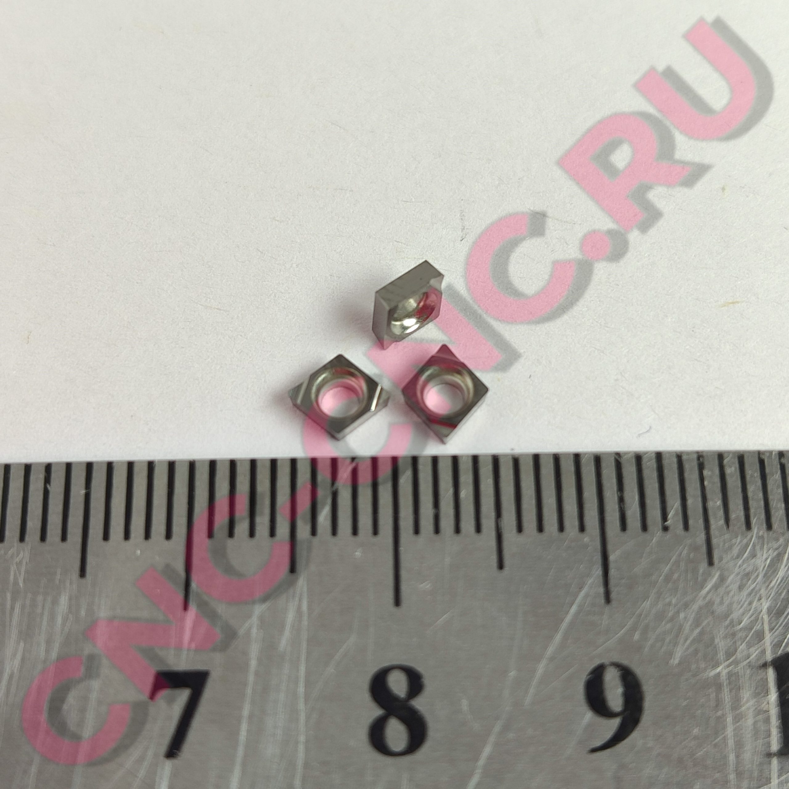 Close-up of a metal ruler with centimeter marks, overlaid by pink decorative text in the background.