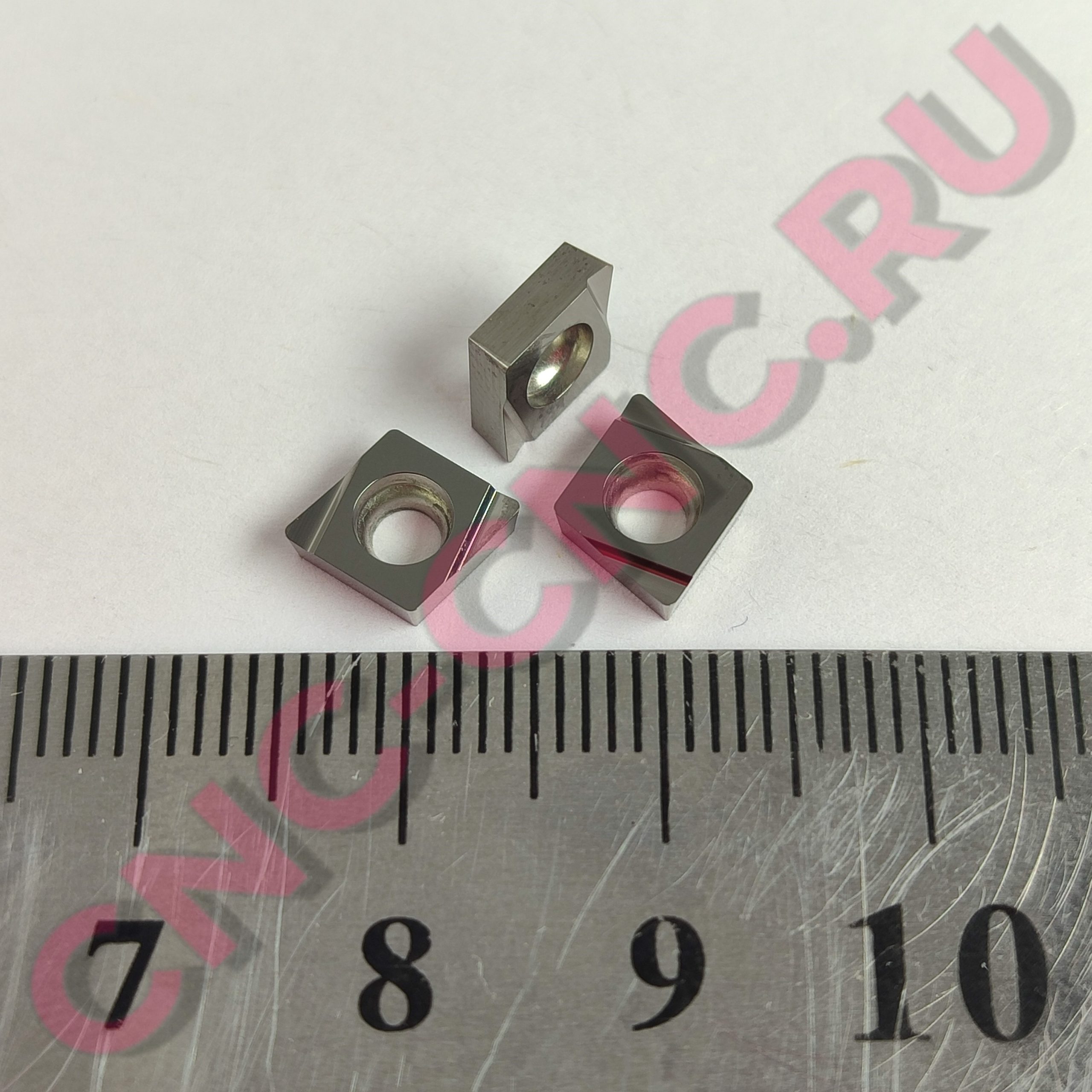 Close-up of a small metal bracket with a circular hole, resting on a ruler for scale.