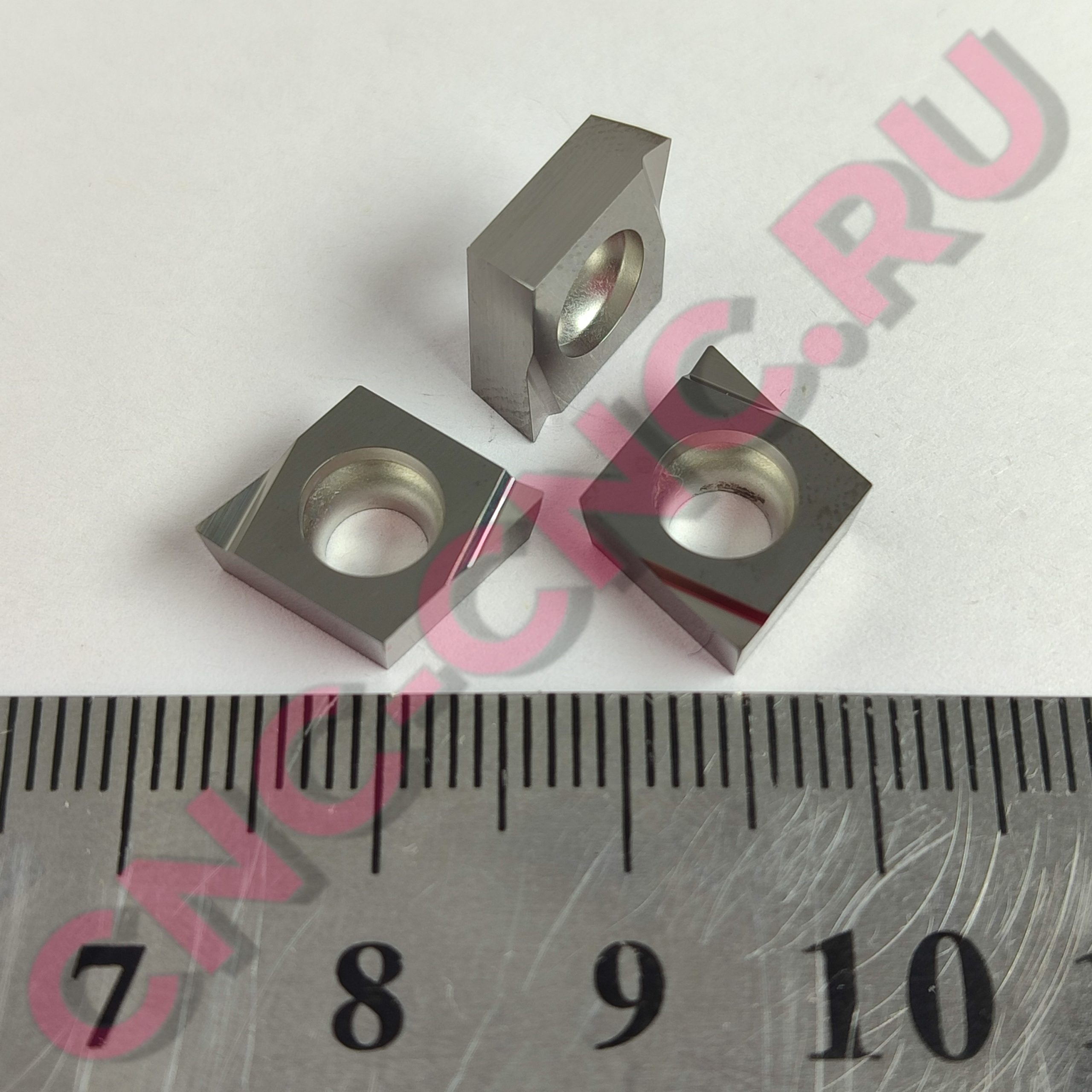 Close-up of gray metal blocks with circular holes on a ruler background, pink watermark text overlay.