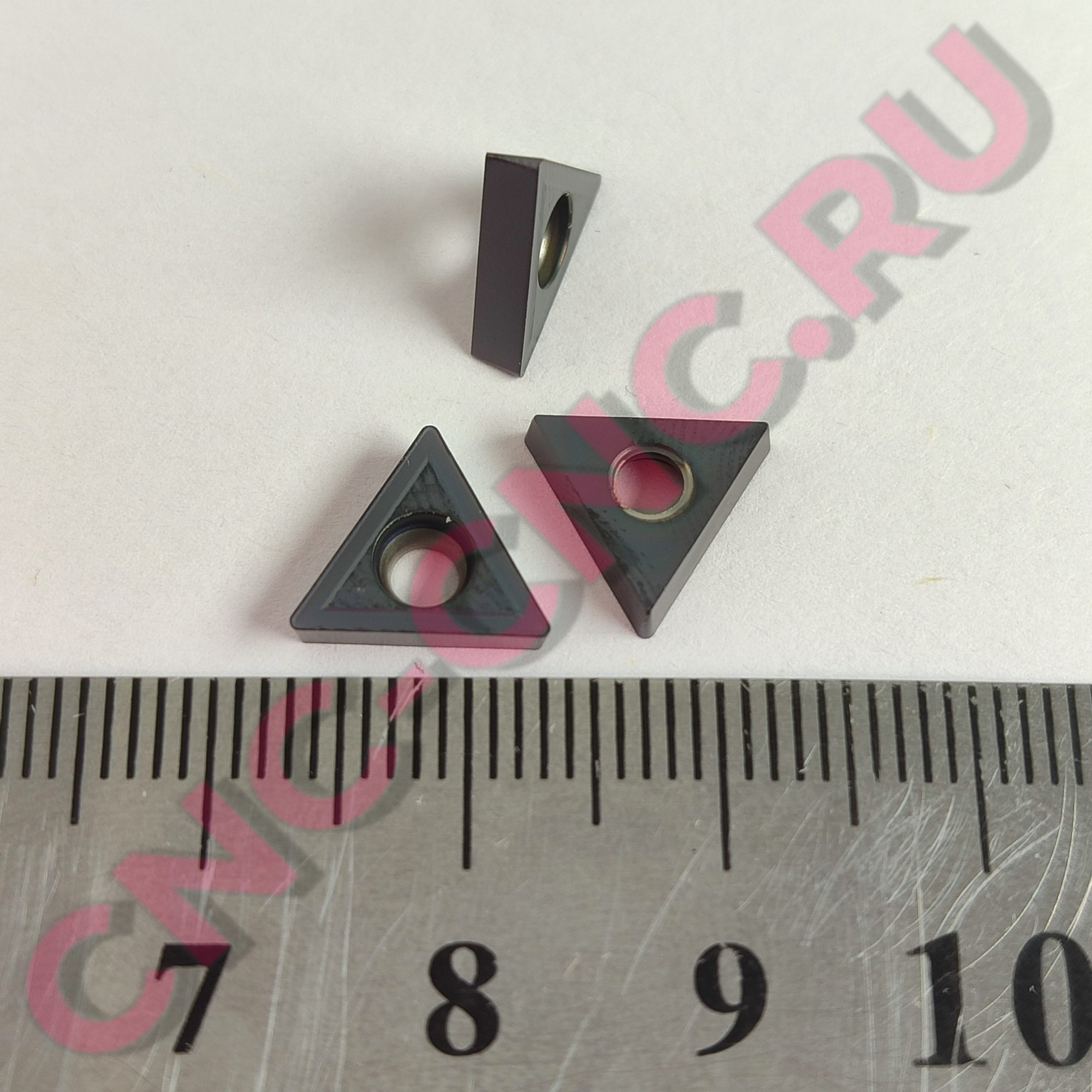 Dark gray triangular plastic brick with a circular through-hole, placed on a ruler