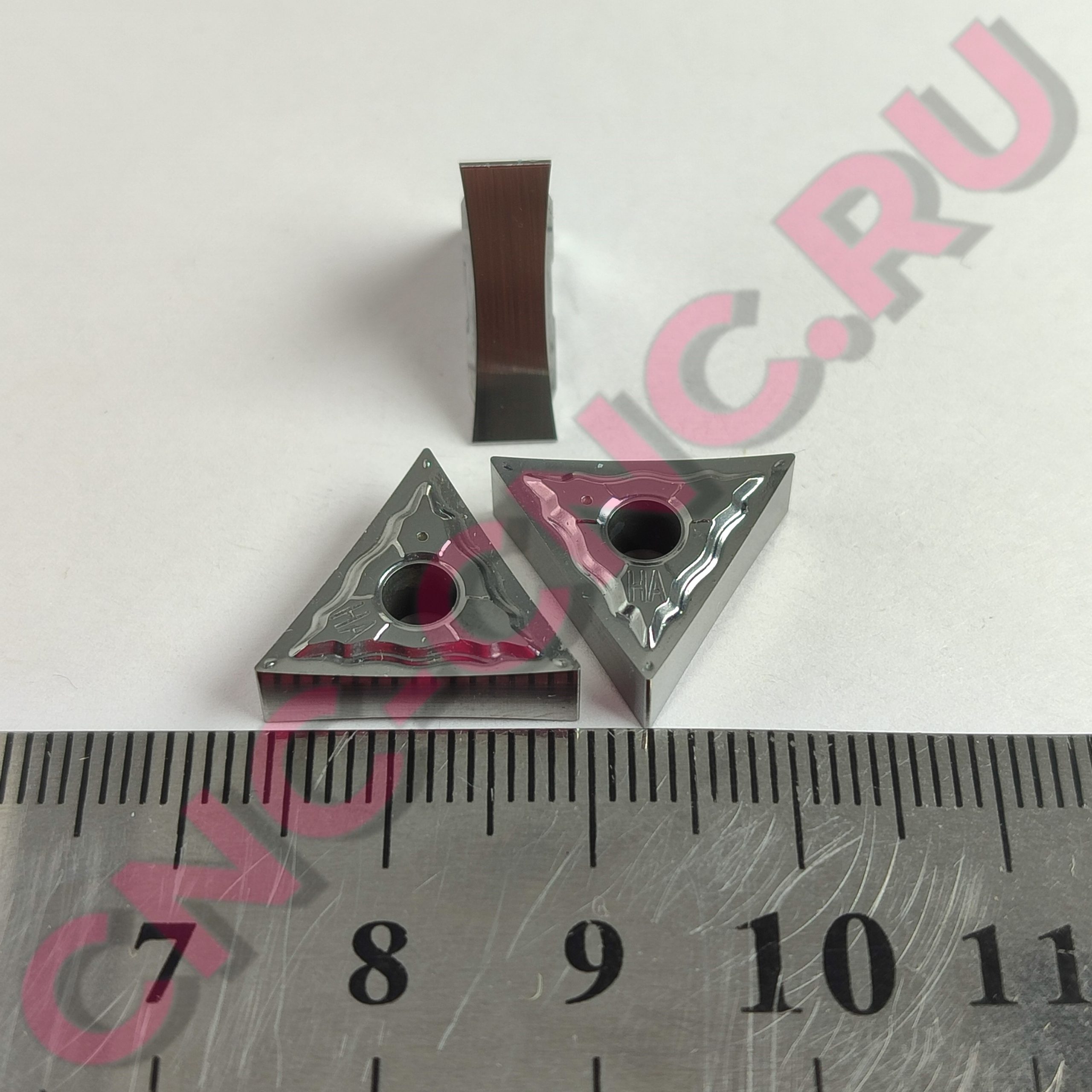 Close-up of a narrow brown wooden strip held upright by metal clamps, with a ruler in the foreground for scale.