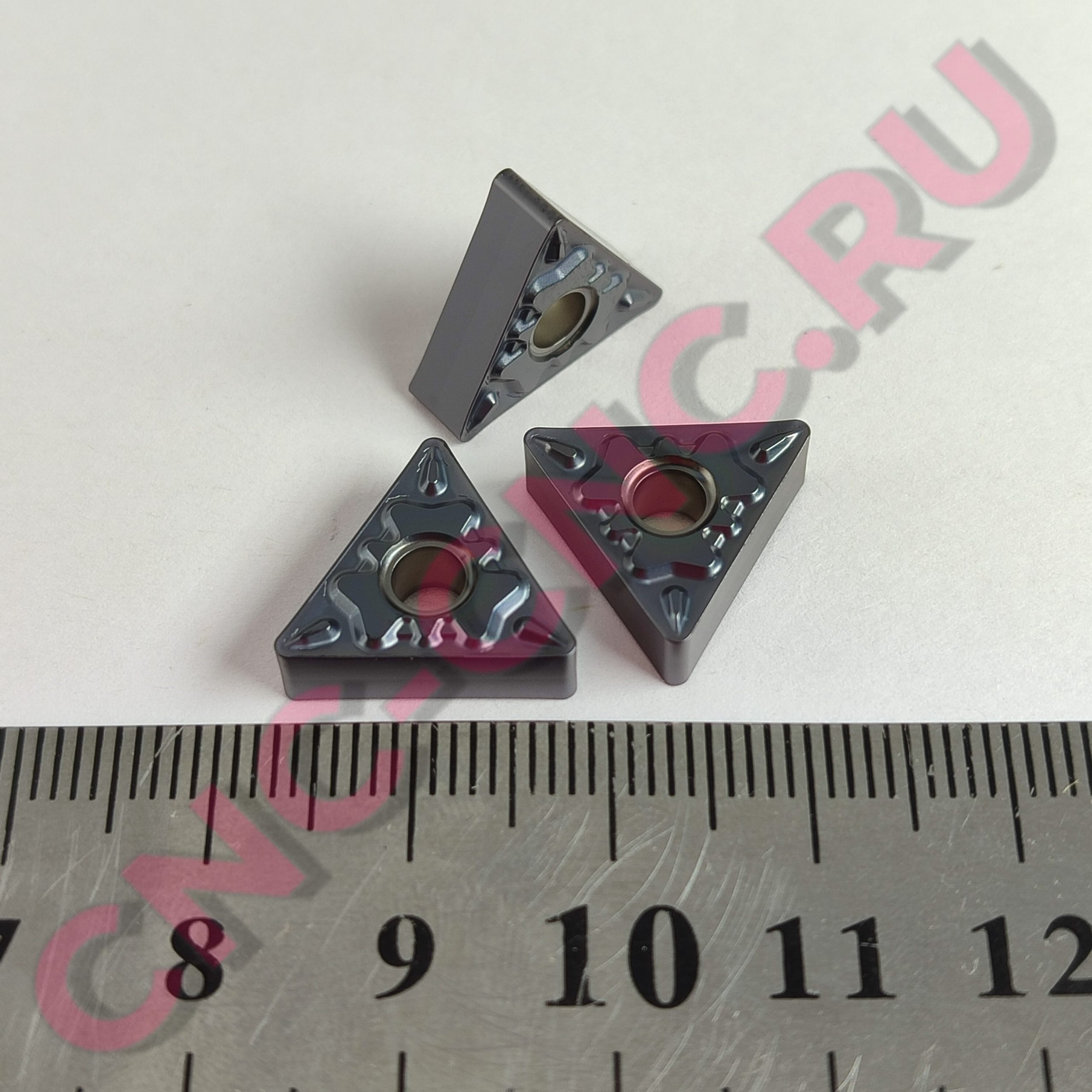 Dark gray square bricks with round central holes laid on a ruler for size reference, close-up shot.