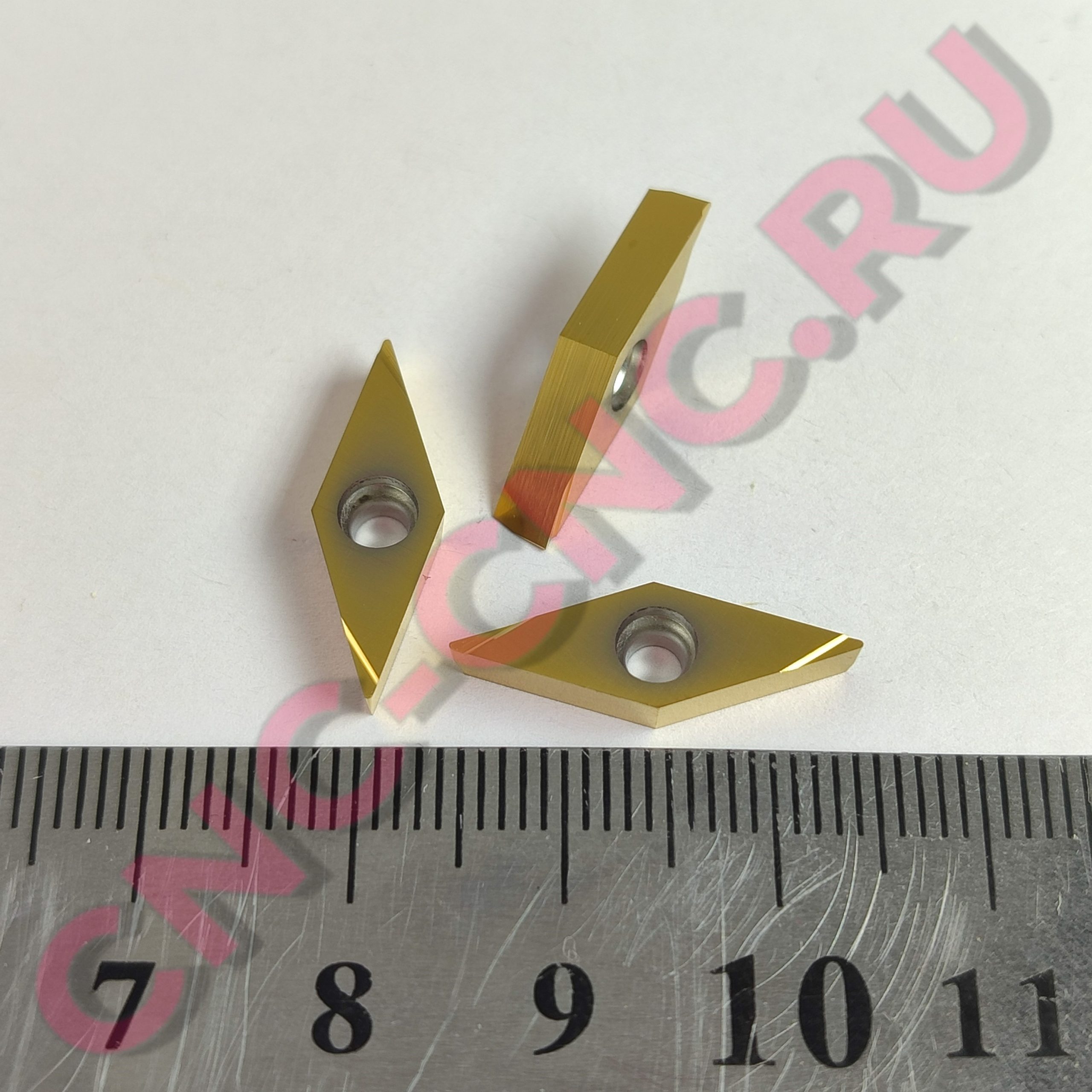 Close-up of a gold-colored metal corner clamp with two bolt holes on a pale surface, with a ruler at the bottom for scale.