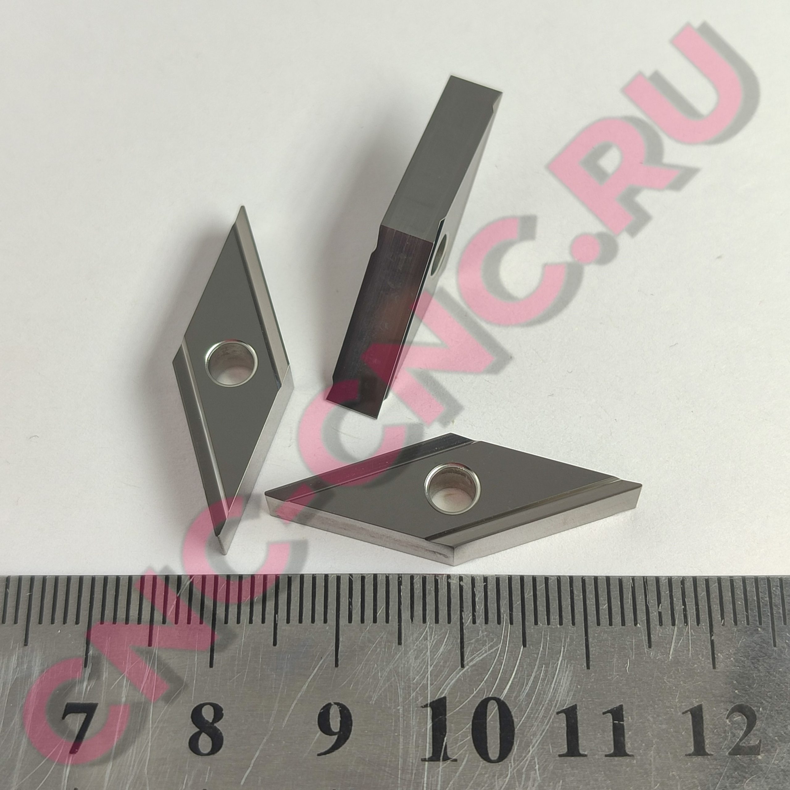 Close-up of a metal mounting bracket with circular holes overlapping a ruler marked in centimeters, with a pink watermark visible across the image.