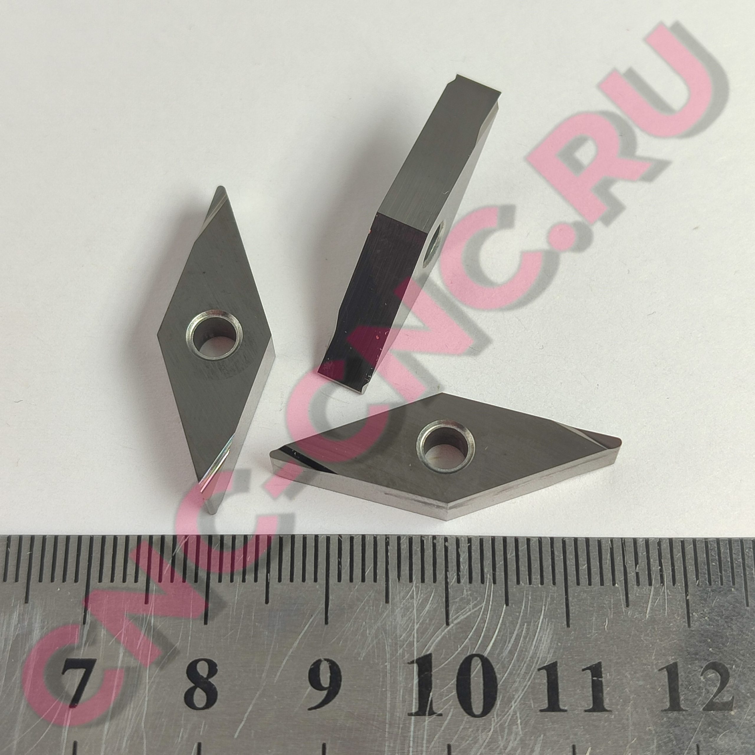 Close-up of metal clamp pieces resting on a marked ruler with metric measurements visible, watermark overlay in pink.