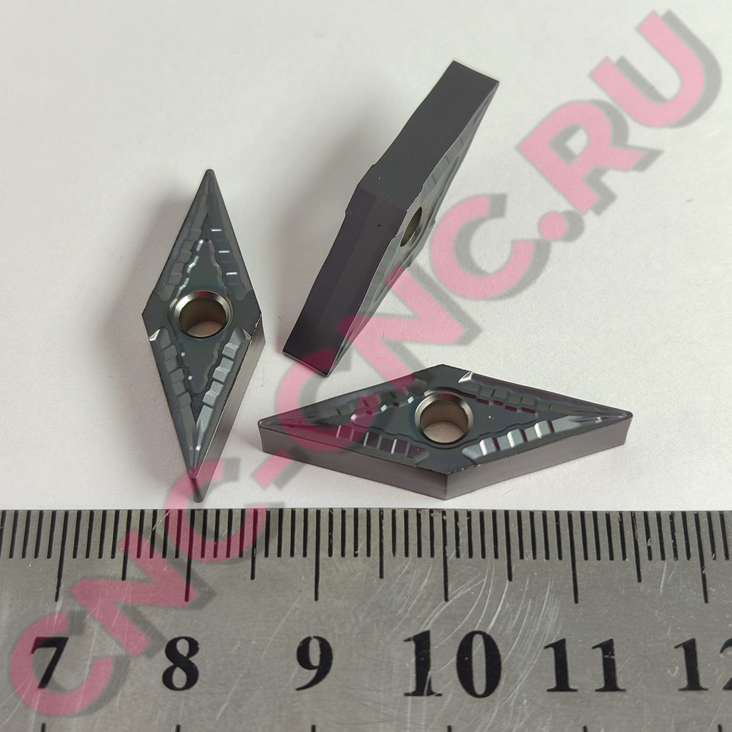 Close-up of three gray plastic clamps with round holes, laid on a ruler.